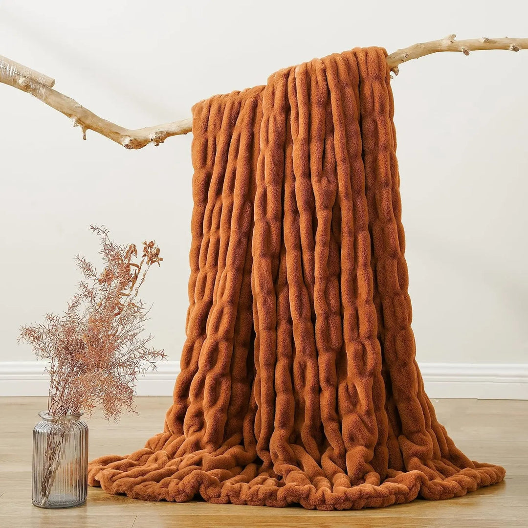 Brown textured blanket draped over a branch with a vase of dried flowers on a light wooden floor.