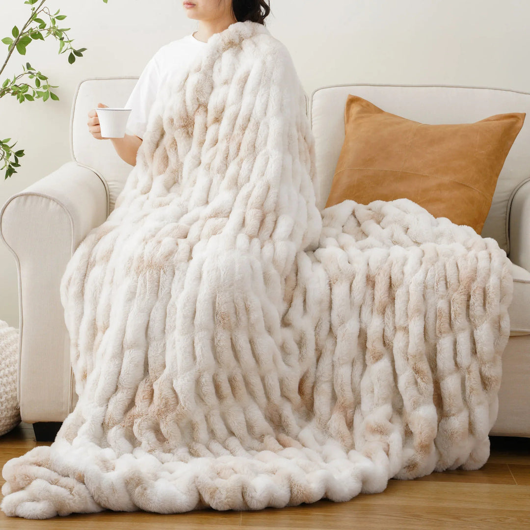 Person sitting on a couch with a large fluffy white blanket draped over them, holding a mug.