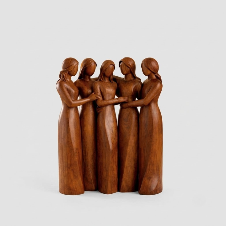A carved wooden sculpture of five women standing together in long dresses, shown against a plain light gray studio background.
