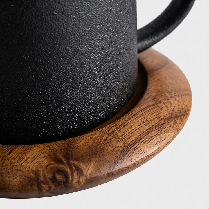Close-up of a black textured mug resting on a round wooden coaster against a light gray background.