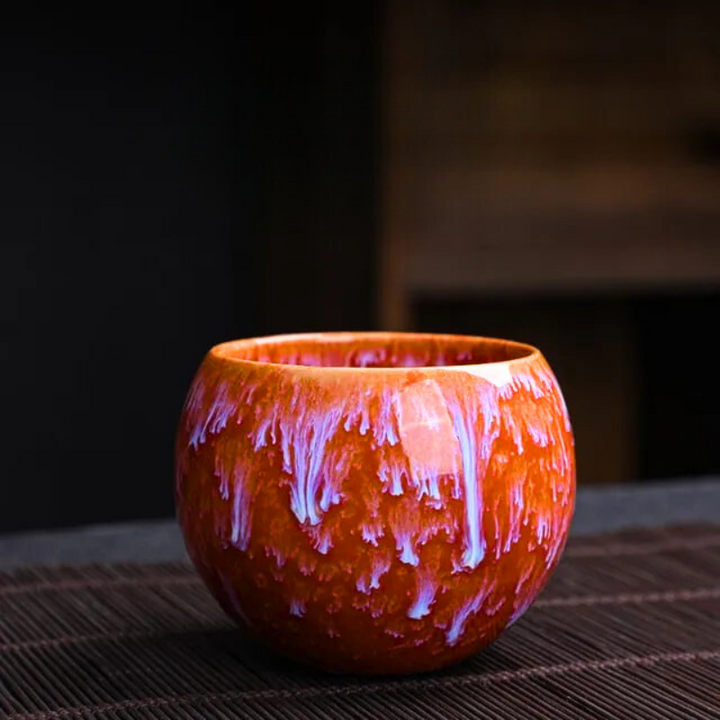 Ceramic cup with orange and purple glaze on a dark background