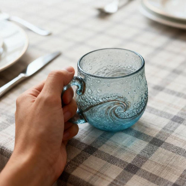 Hand holding a textured glass mug on a checkered tablecloth