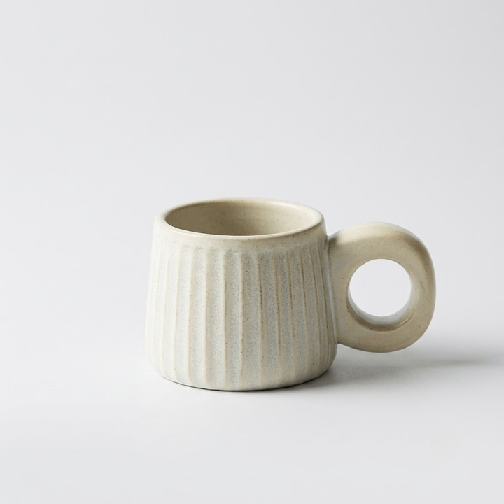 A light beige ceramic mug with a ribbed body and a loop handle, photographed on a clean white background.