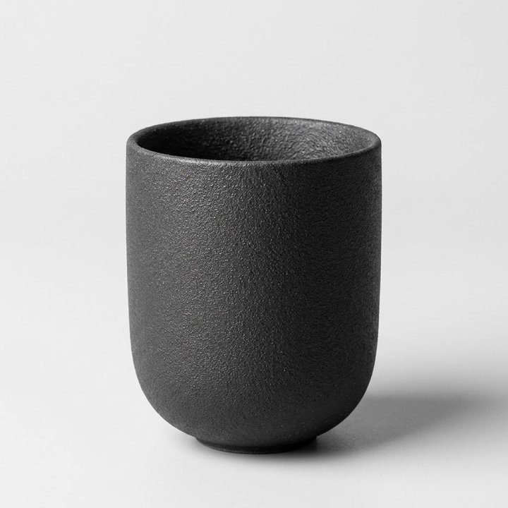 A matte black textured ceramic cup with a rounded, tapered shape, shown on a light gray background.
