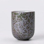 A ceramic cup with a textured, speckled glaze in metallic silver, olive green, and dark brown, set against a plain light gray background.