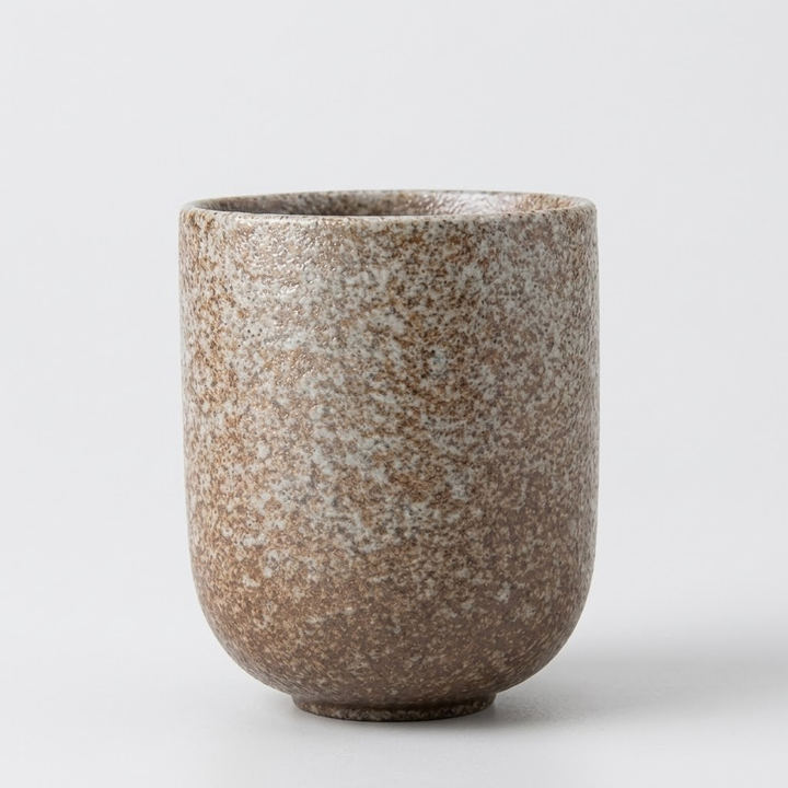 A speckled ceramic cup with a textured brown and beige glaze, shown on a clean light gray background.