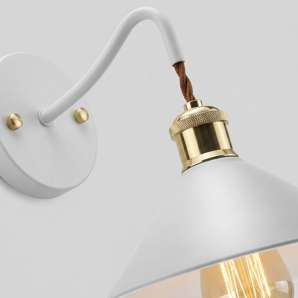 A close-up of a modern wall sconce with a matte white curved arm and shade, brass hardware, and a brown woven fabric cord, shown against a light gray background.
