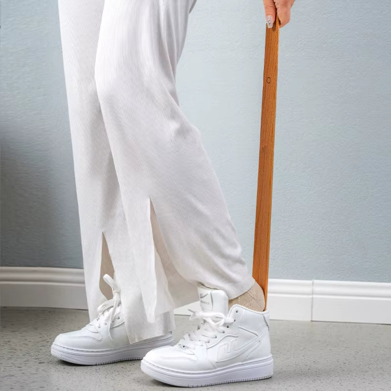 Person wearing white sneakers and light-colored pants holding a wooden object against a neutral background