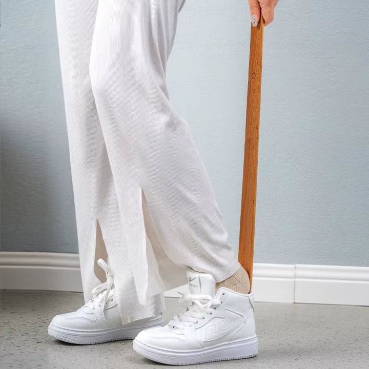 Person wearing white sneakers and light-colored pants holding a wooden object against a neutral background