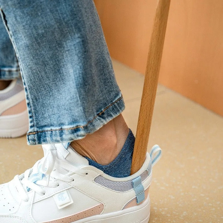 White sneakers with blue accents worn with rolled-up jeans on a beige floor.