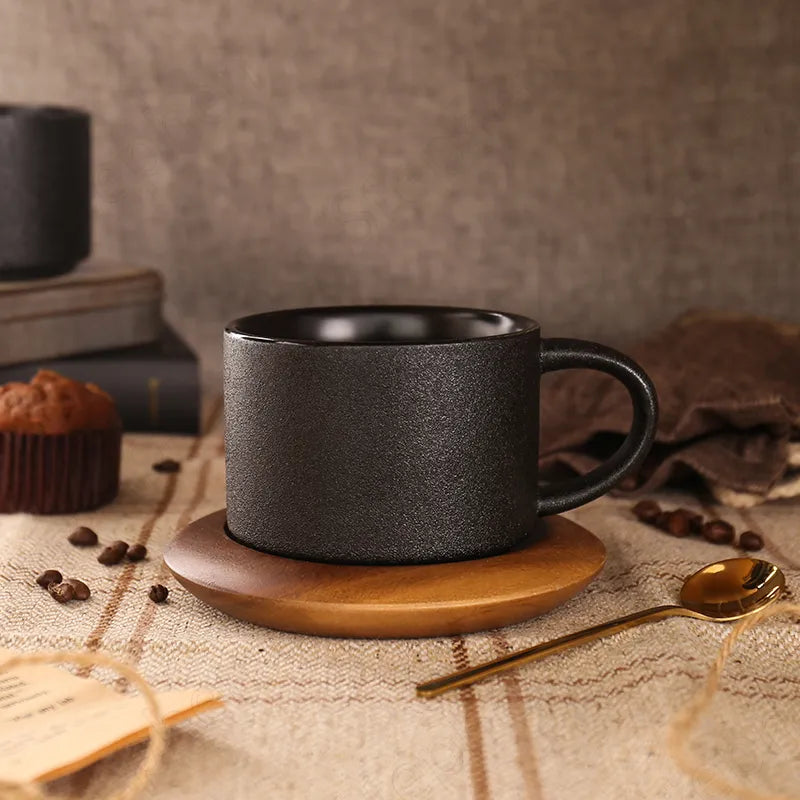 Black mug on a wooden coaster with coffee beans and a spoon on a textured surface.