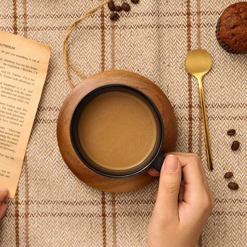 Hand holding a wooden mug with coffee, surrounded by coffee beans, a gold spoon, and a book on a textured fabric background.