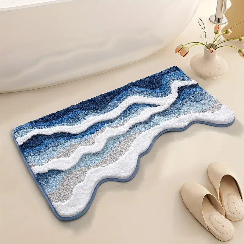 Blue and white wavy patterned bath mat on a bathroom floor with a vase and slippers in the background.