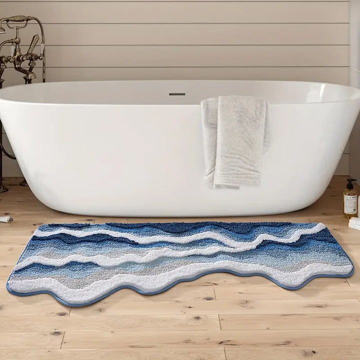 Blue wavy-patterned bath mat in front of a white freestanding bathtub.