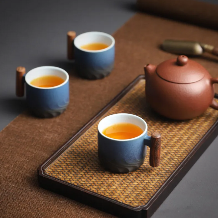 Tea set with a teapot and three cups on a woven tray.