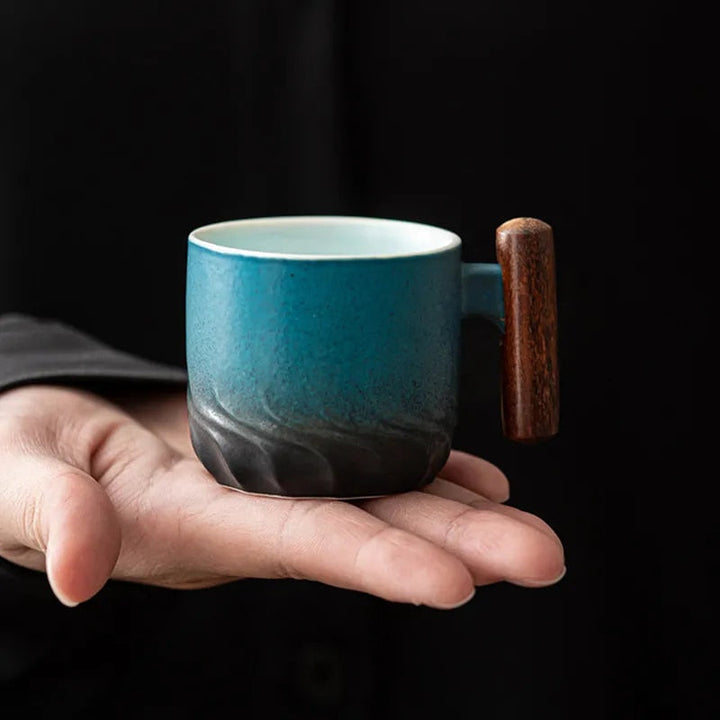 Blue ceramic mug with a wooden handle held in a hand against a black background