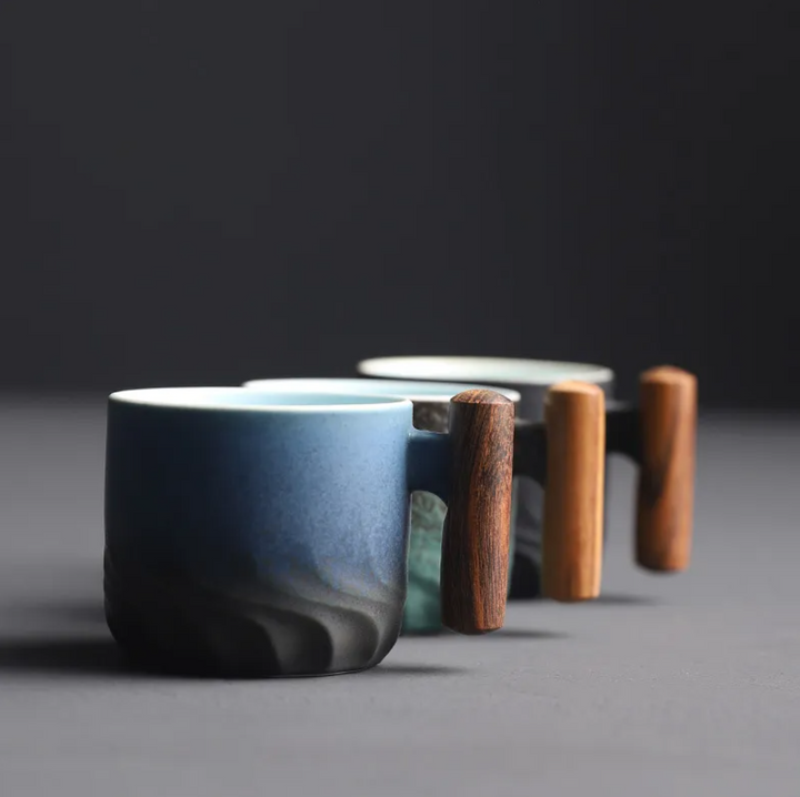 Three ceramic cups with wooden handles on a dark background