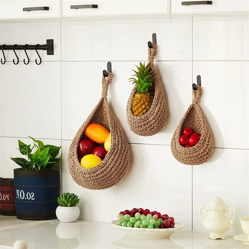 Three woven fruit holders hanging on a kitchen wall with fruits inside.