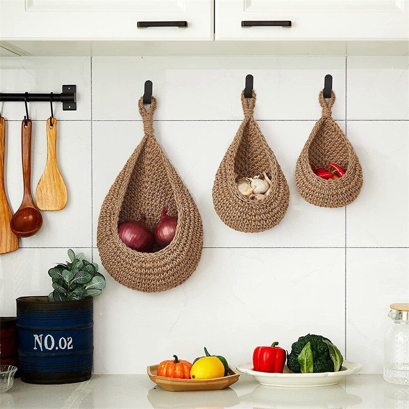 Three woven fruit holders hanging on a kitchen wall with vegetables below.