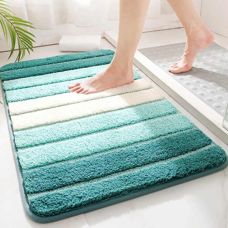 A striped bath mat in shades of teal, mint, and cream, shown in a bathroom with a person's bare feet stepping onto it.
