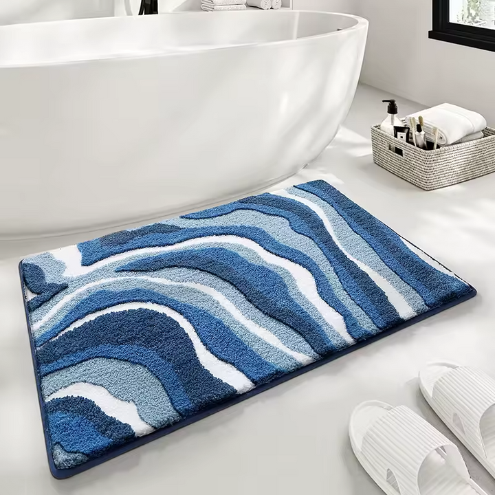 Blue and white patterned bath mat on a bathroom floor with a bathtub and basket in the background.