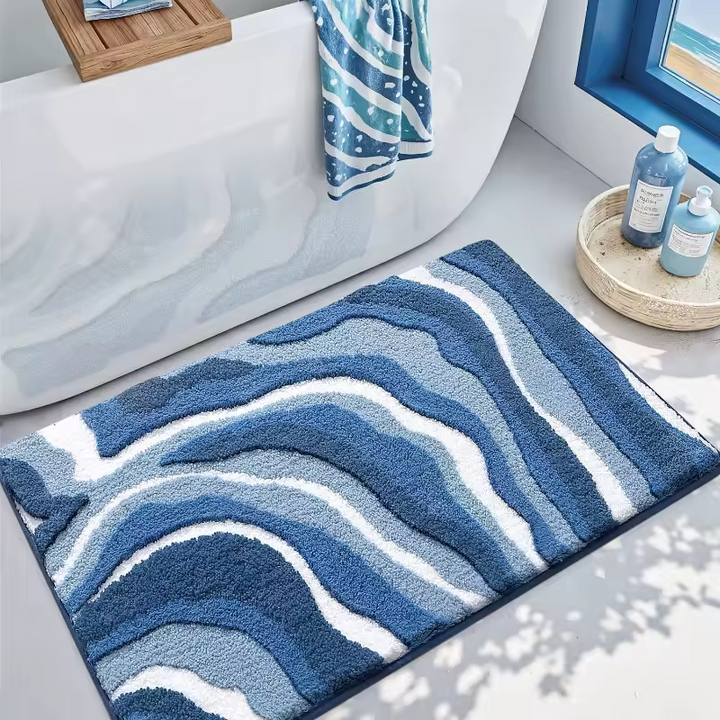 Blue and white wavy patterned bath mat in a bathroom setting with a bathtub and towels.