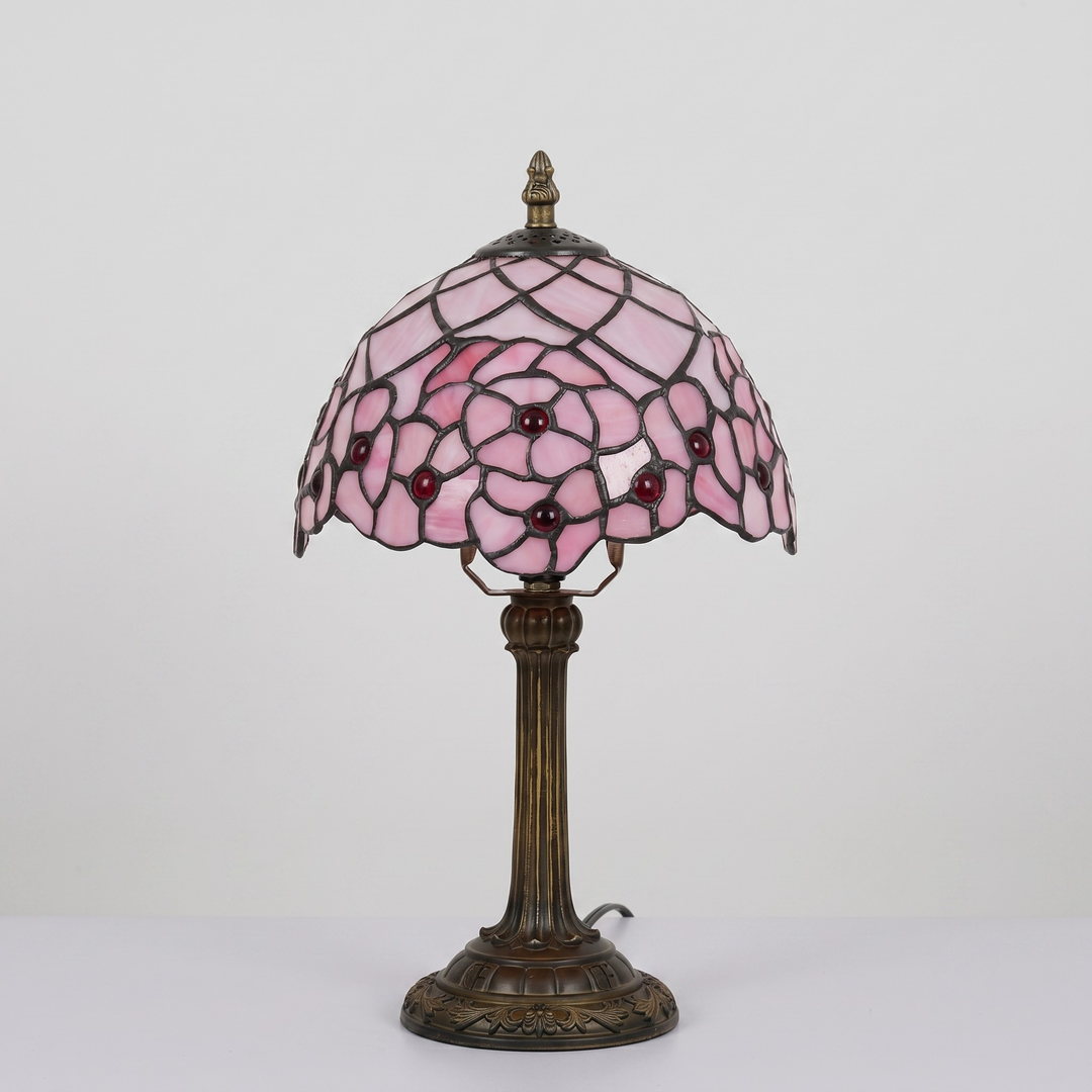 A Tiffany-style table lamp with a pink stained glass shade featuring a floral pattern and a dark bronze metal base.