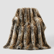 A plush faux fur throw blanket draped over a chair, showcasing a realistic brown, beige, and gray animal print pattern, set against a plain light gray background.