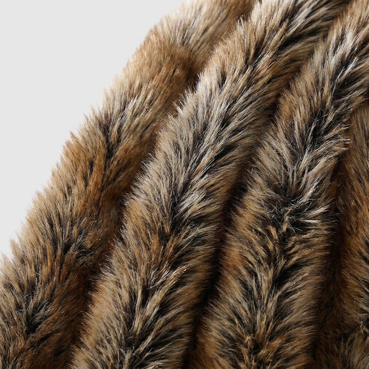 A close-up of a plush faux fur or animal-print textile with layered shaggy texture in warm brown, tan, black, and cream tones against a light gray background.