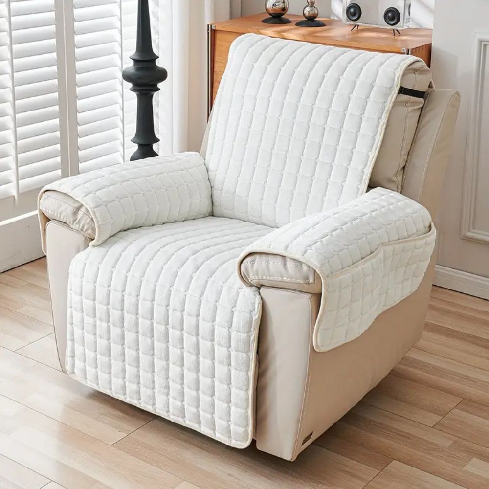 Beige recliner chair with a white quilted cover in a room with wooden flooring and a window.