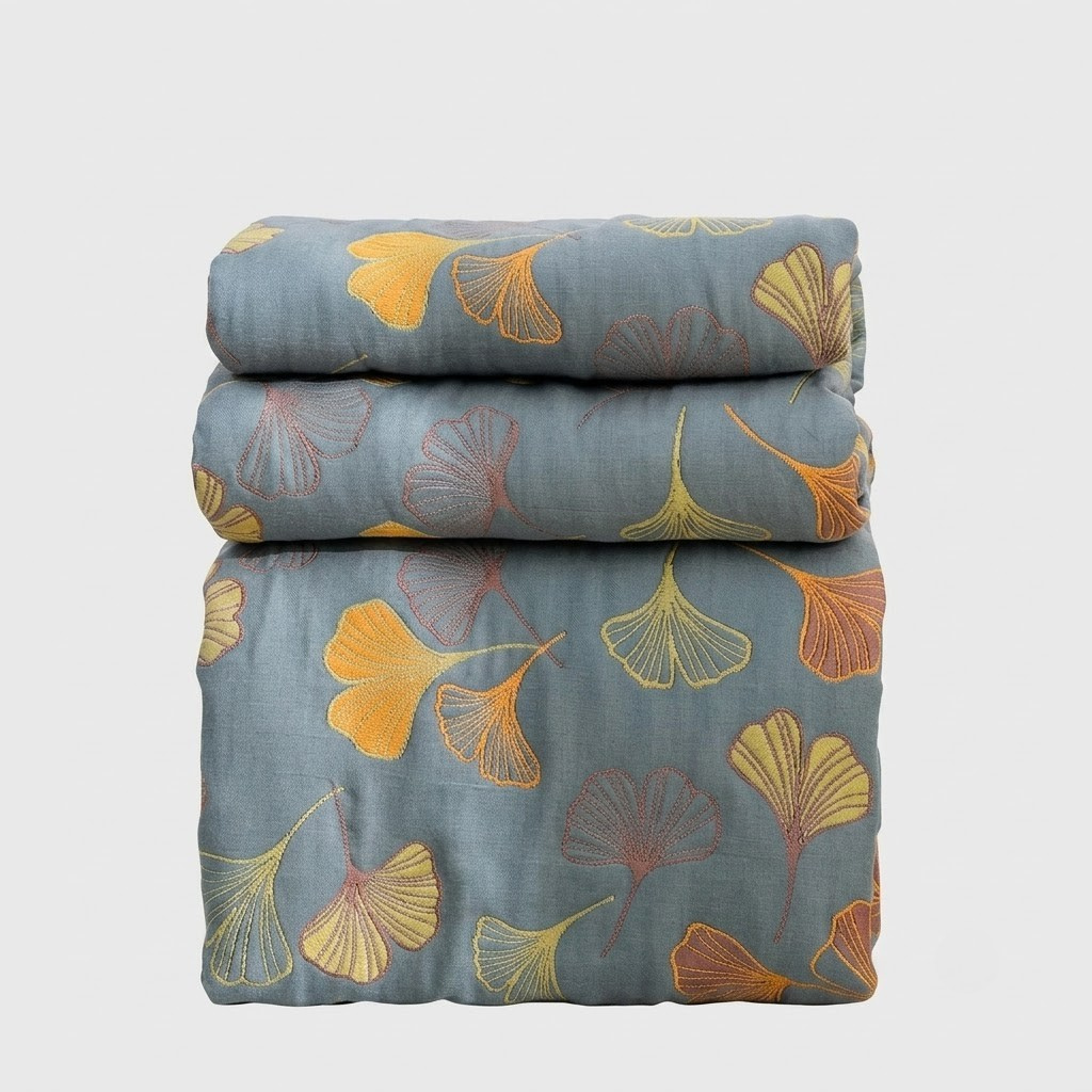 A folded stack of three bedding items, likely a duvet cover or comforter set, featuring a muted slate blue-gray background with a pattern of yellow, orange, and red ginkgo leaves.