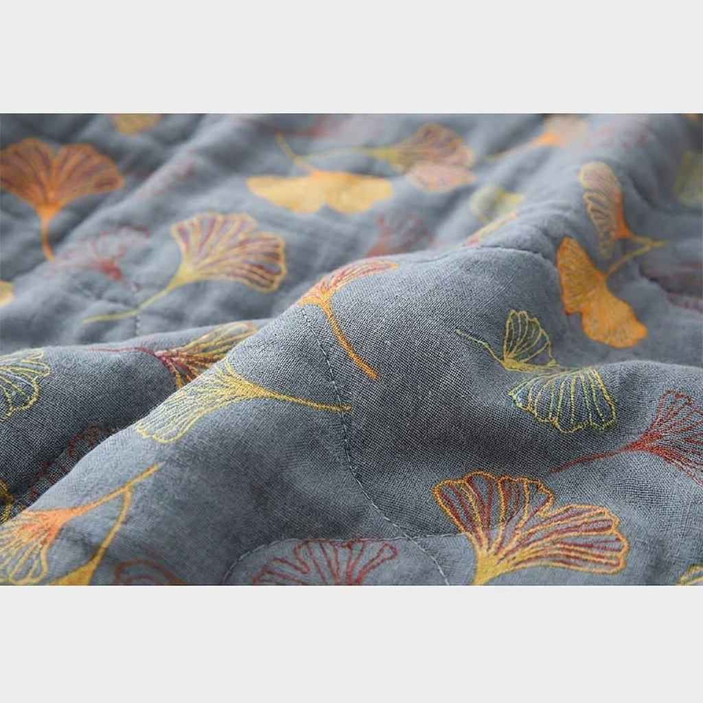 A close-up of a quilted fabric featuring a gray base with embroidered ginkgo leaves in yellow, orange, and red.