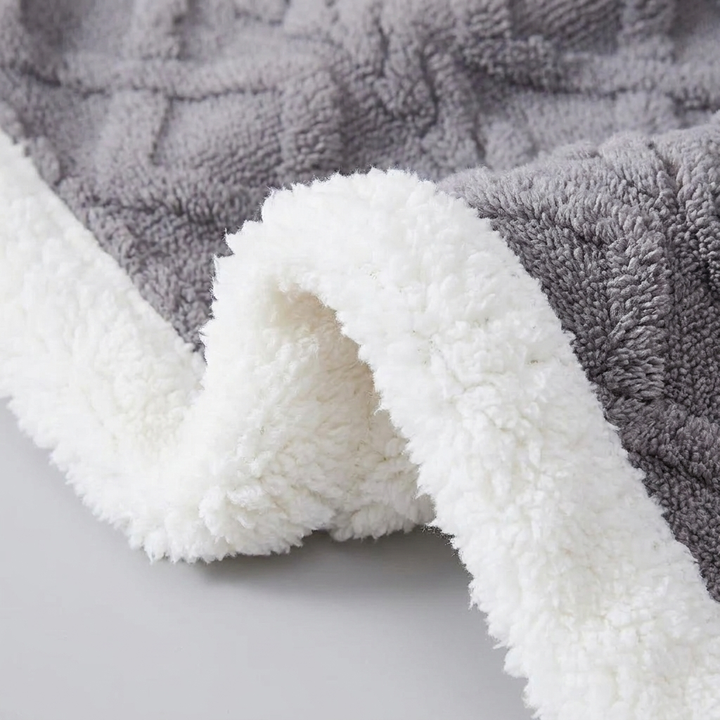 Close-up of a plush fleece blanket with a gray textured side and a soft white sherpa lining, folded over to show the reversible material.