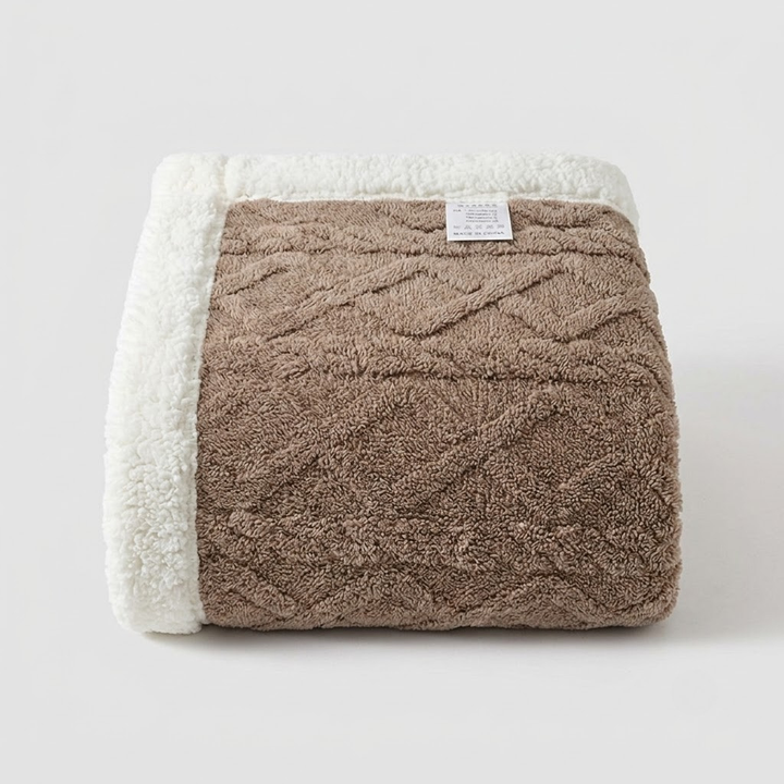 A folded textured blanket with a brown diamond-patterned center and a white sherpa fleece border, shown on a light gray background.
