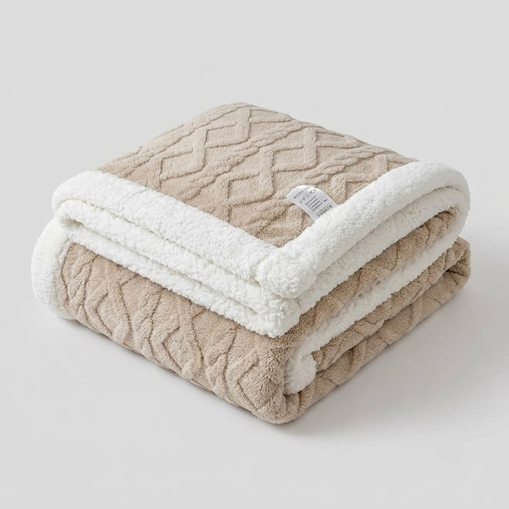 A folded plush throw blanket with a textured beige geometric pattern and a thick white sherpa lining, shown on a light gray background.