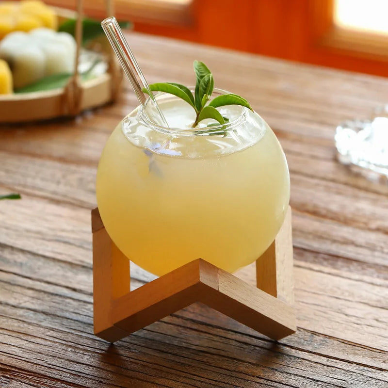 Yellow drink in a glass with a straw and mint leaf on a wooden stand, set on a wooden table.