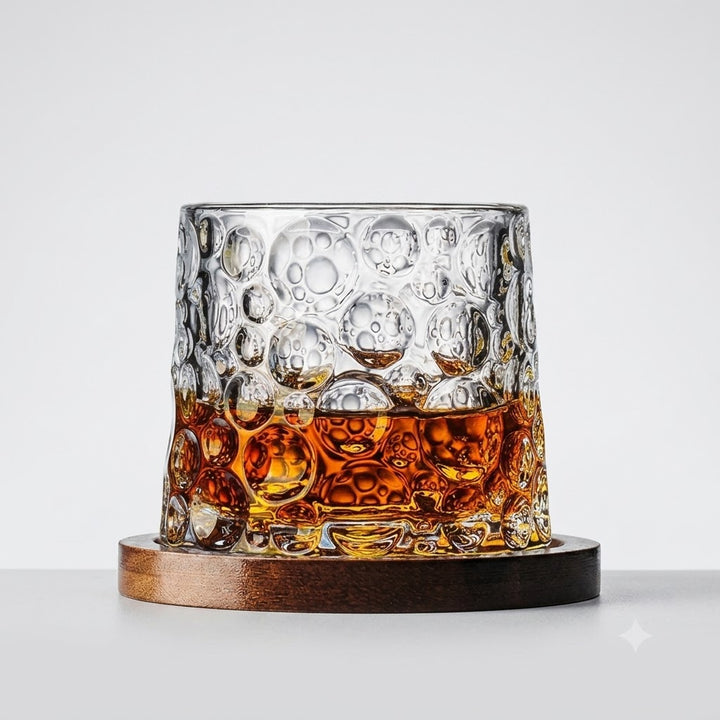 A clear textured glass tumbler with a bubble pattern, partially filled with amber whiskey, resting on a round dark wooden coaster against a light gray background.