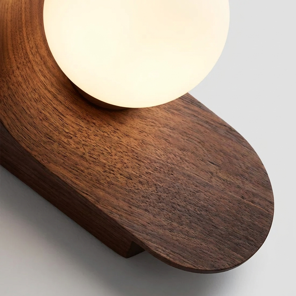 Close-up of a modern wall lamp with a curved dark wood base and a glowing frosted white globe shade, shown against a light gray background.