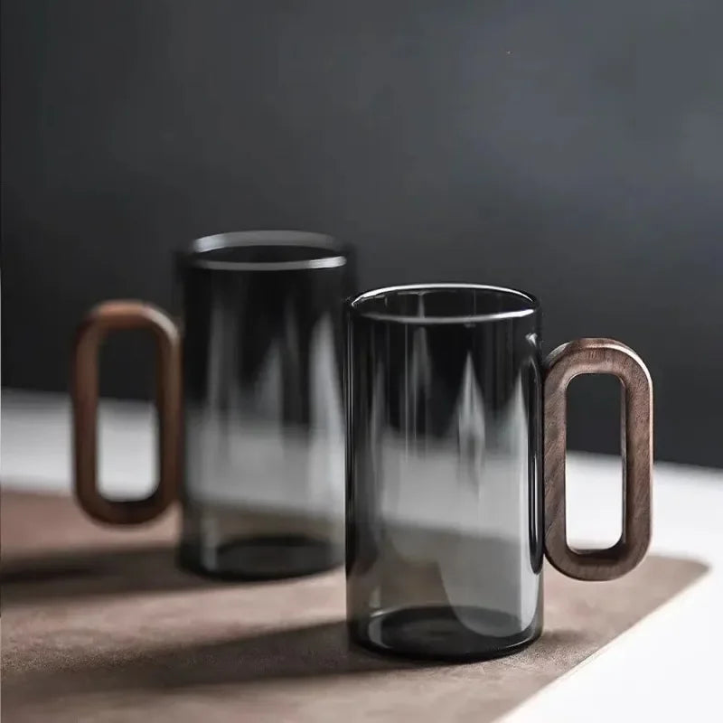 Two smoked glass mugs with wooden handles on a dark surface.