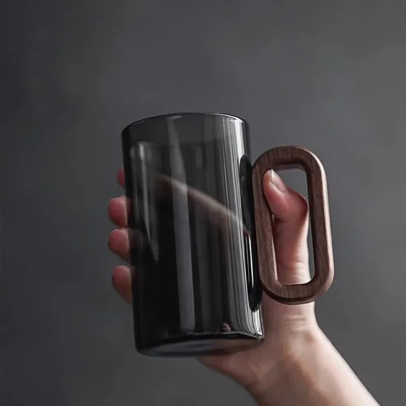 Black mug with a wooden handle held by a hand against a dark background