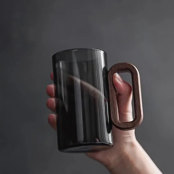 Black mug with a wooden handle held by a hand against a dark background