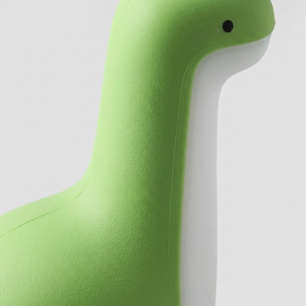 Close-up of a green and white duck-shaped chair or stool with a small black eye detail, shown against a plain light gray background.