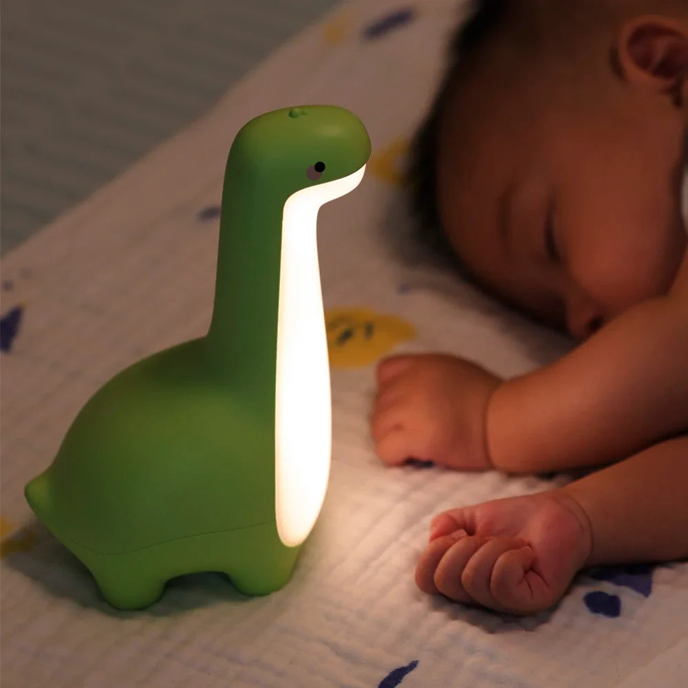 Green dinosaur-shaped night light next to a sleeping baby
