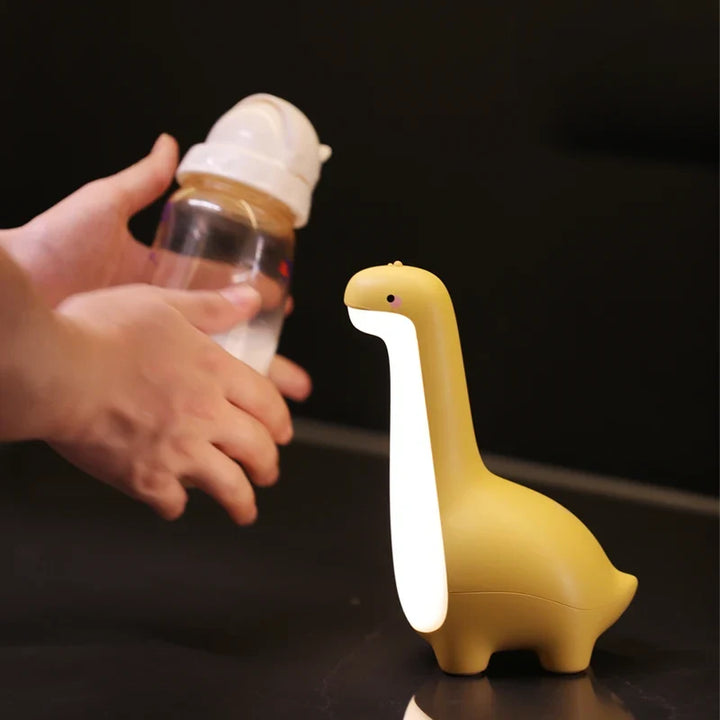 Yellow dinosaur-shaped night light next to a hand holding a bottle on a dark surface.