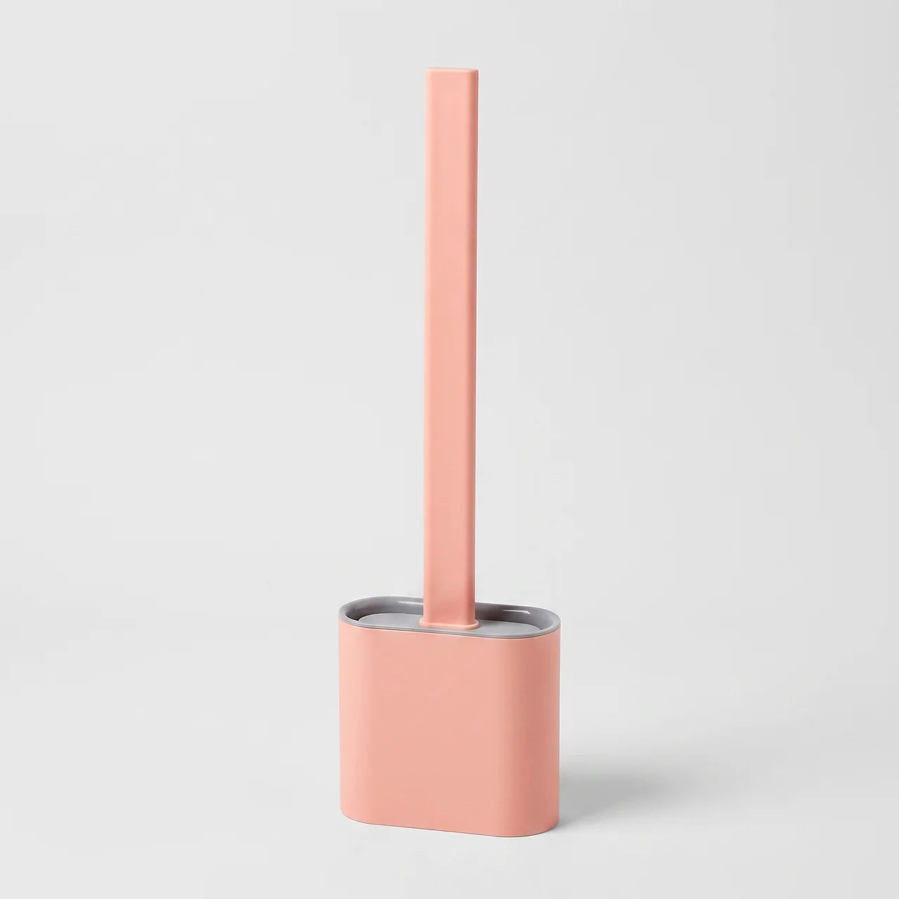 A minimalist toilet brush with a tall, slim handle and a rounded rectangular base, shown in a solid pastel pink color with a silver metallic inner rim, set against a clean light gray background.