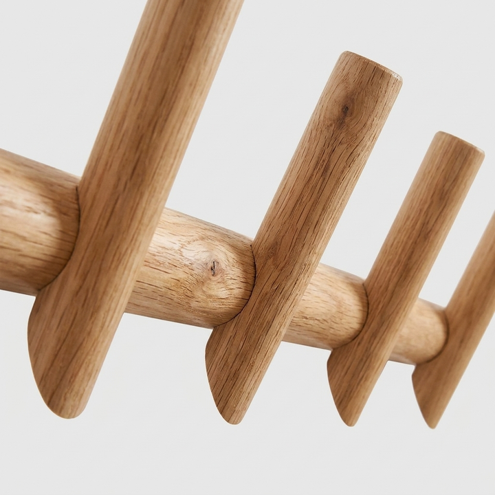 Close-up of a light natural wood coat rack with rounded pegs and a smooth horizontal bar, shown against a plain light gray background.