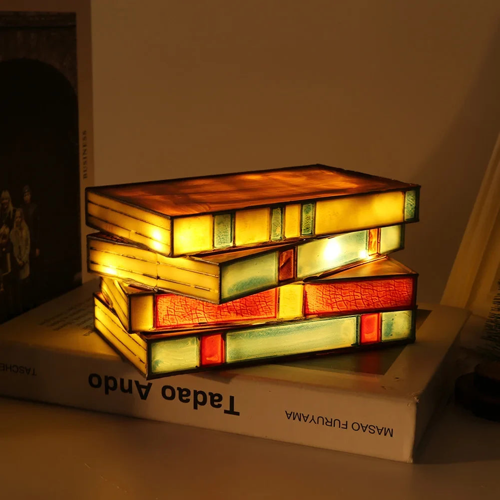 Stack of colorful books illuminated from within, resembling a lamp, on top of a book titled 'Tadao Ando' by Masao Furuya.