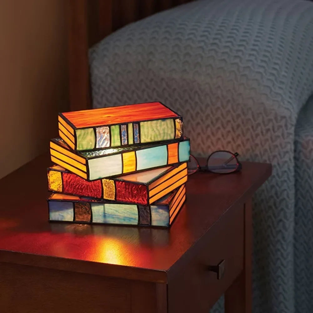 Stack of colorful stained glass books on a wooden surface with a chair in the background.