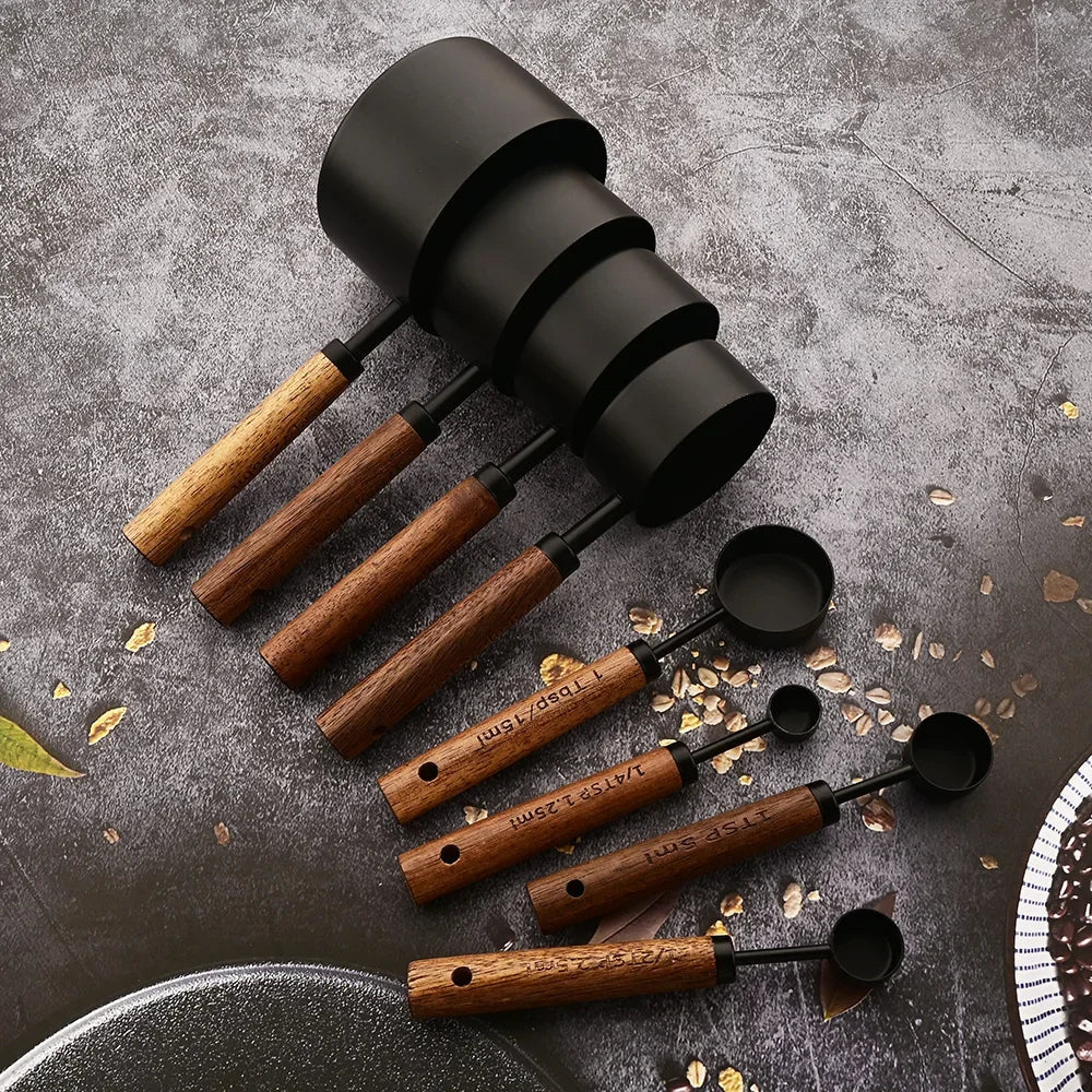 Set of black and wooden measuring spoons on a textured surface with oats.