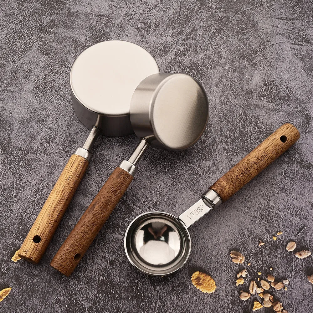 Three metal measuring cups with wooden handles on a gray surface.